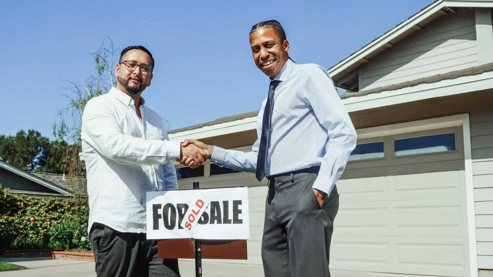 Real estate agent shaking hands with a homebuyer in front of a sold house sign, representing successful real estate lead conversion.