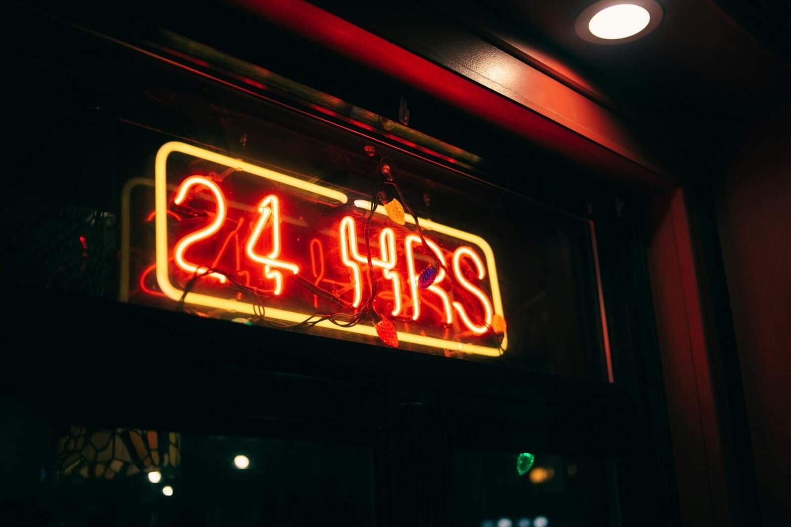 A glowing red neon sign that says "24 HRS" in a window, representing the round-the-clock availability provided by AI conversational systems for global real estate leads.