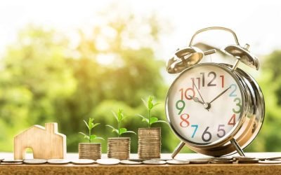 Real estate revenue growth concept with alarm clock, stacked coins with plants, and wooden house symbolizing time and investment returns